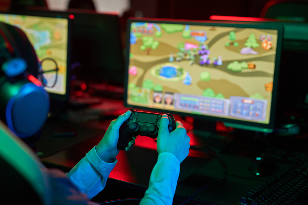 Persona jugando a un videojuego con mando frente a un monitor, en un entorno iluminado con luces de colores.