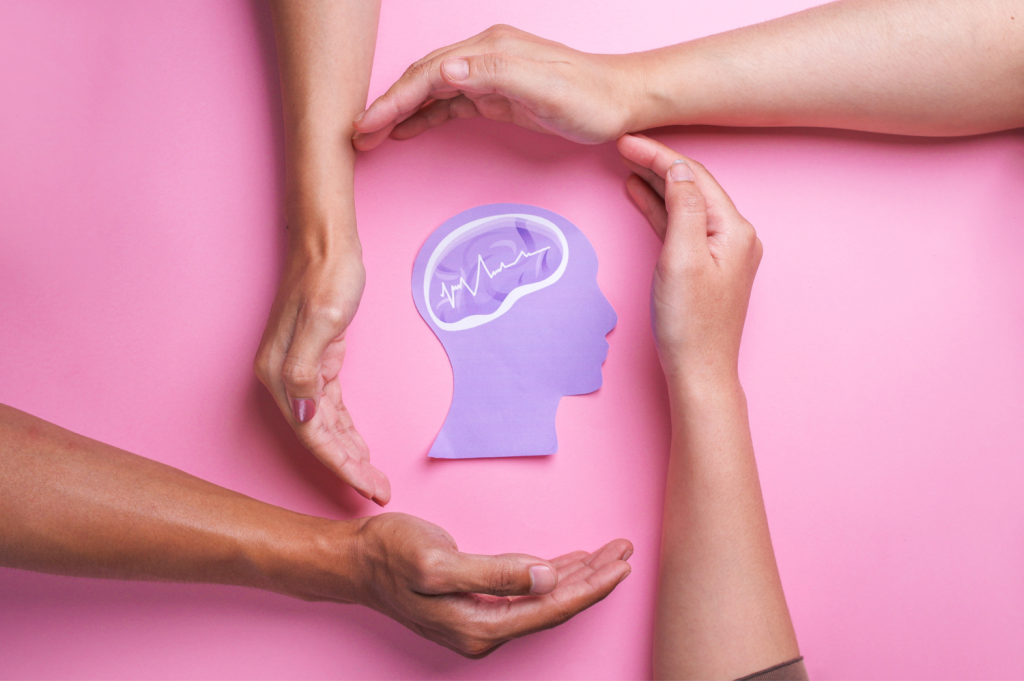 Manos rodeando la silueta de una cabeza con un cerebro ilustrado, simbolizando cuidado y apoyo a la salud mental.